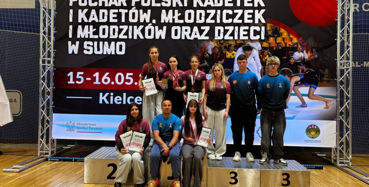 Sześć dziewczyn i dwóch chłopaków w jednakowych strojach stoją i siedzą z trenerem na podium