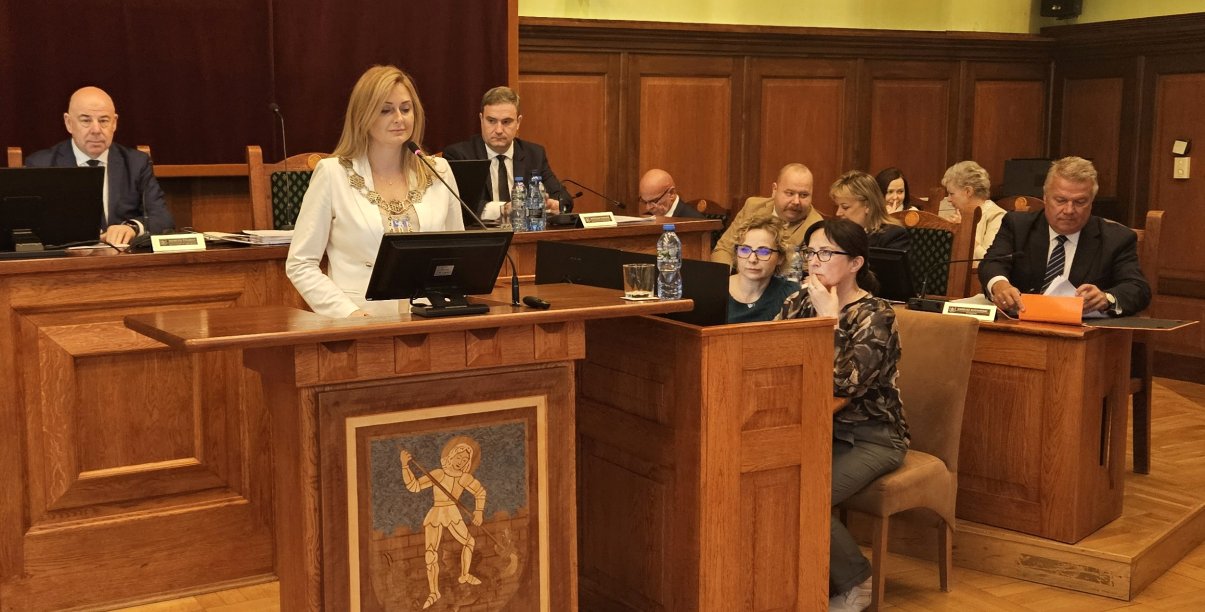 Przewodnicząca rady przy mównicy, za nią przy stole dwóch wiceprzewodniczących, po prawej burmistrz