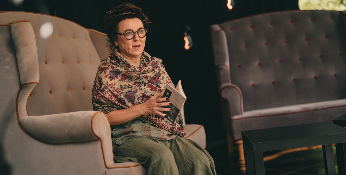Olga Tokarczuk siedząca w duzym fotelu z książką w rękach