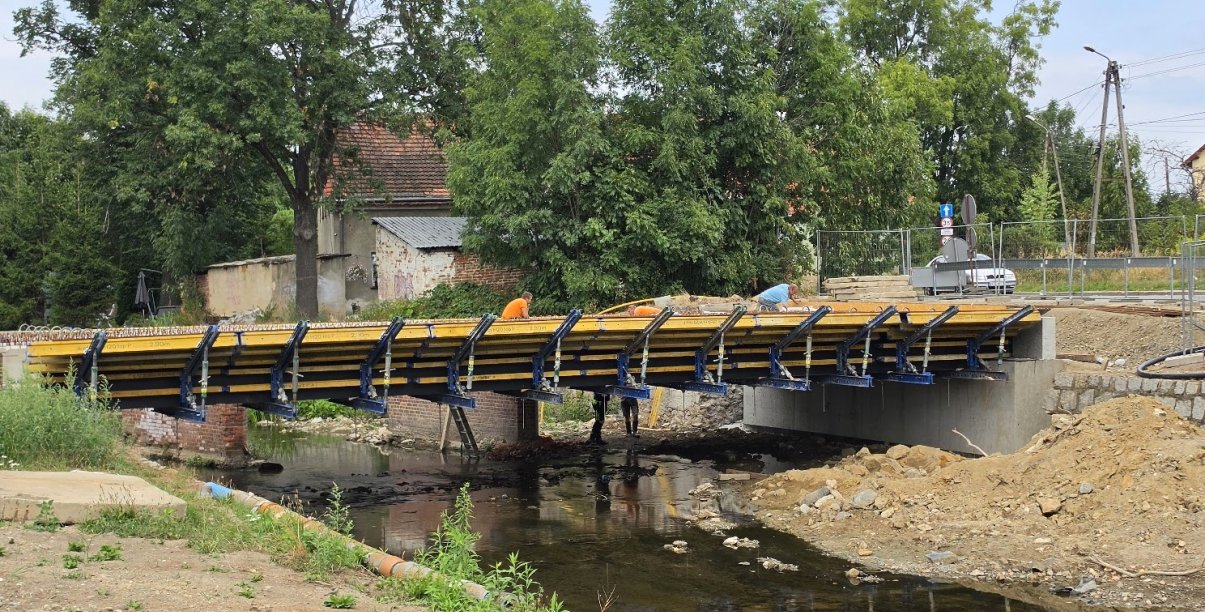 Most w budowie nad niewielką rzeką, w tle drzewa