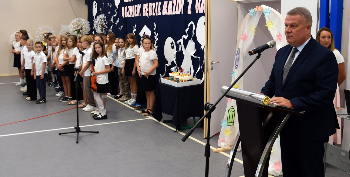 Burmistrz Dzierżoniowa przy mównicy w sali gimnastycznej, obok grupka dzieci