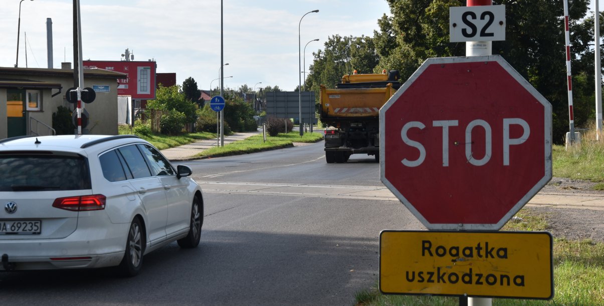 Biały samochód przed przejazdem kolejowym, po prawej znak "Stop"