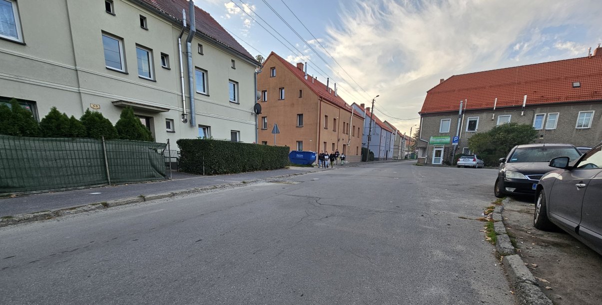 Droga asfaltowa, po bokach domy, chodnikiem idzie grupka dzieci