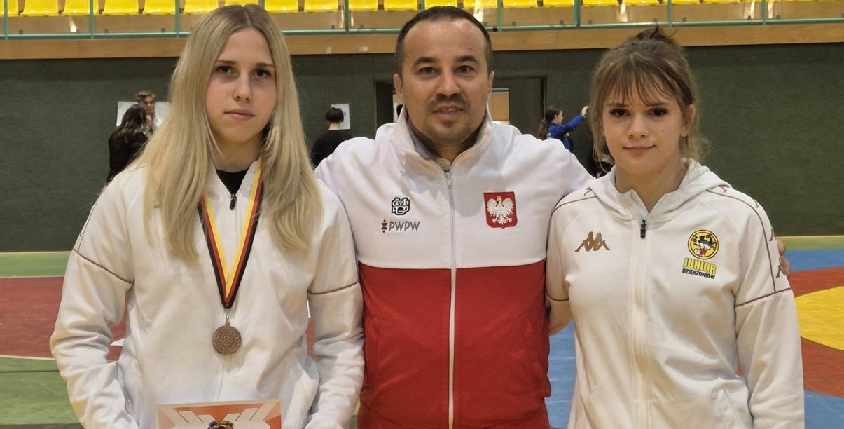 Trener w biało-czerwonej bluzie, po bokach dwie zawodniczki 