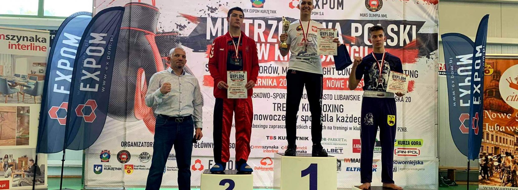 Maksymilian Palej na najwyższym stopniu podium, obok inni zawodnicy i trenerzy