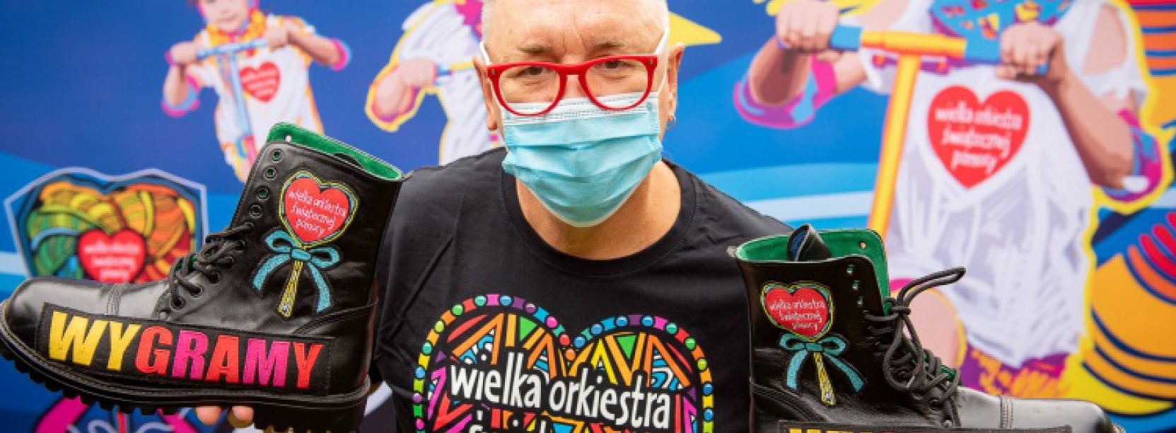 Jerzy Owsiak w maseczce, na tle plakatu WOSP.