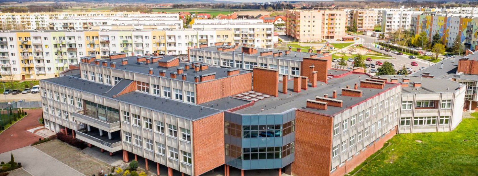 Budynek dużej szkoły, w tle osiedle mieszkaniowe 
