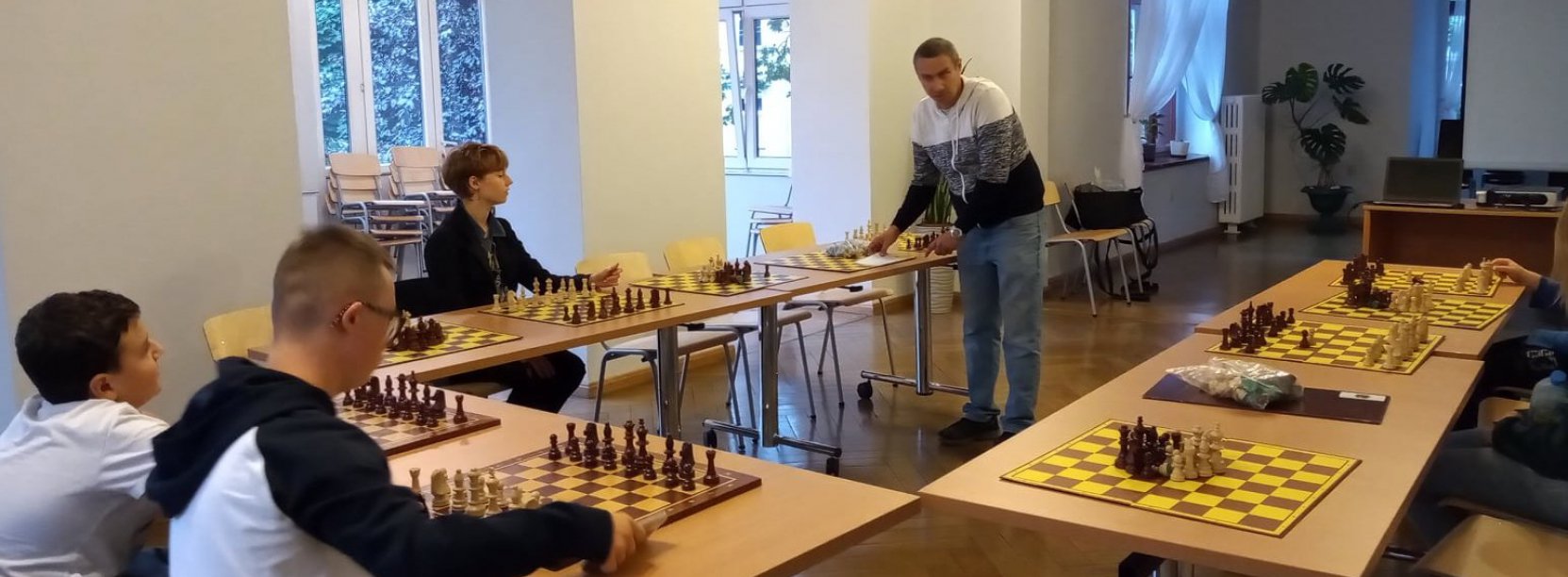 Sala, na stołach rozłożone plansze do szachów, kilka osób przed szachownicami