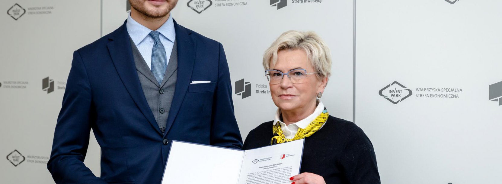 KObieta i mężczyzna trzymaja teczkę z dokumentami na tle ścianki Invest Park