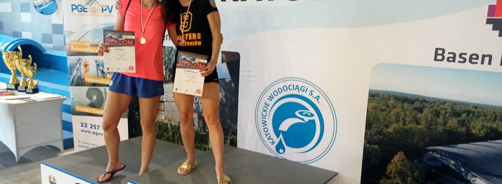 Dwie uśmiechnięte zawodniczki na podium, obok napis Katowice