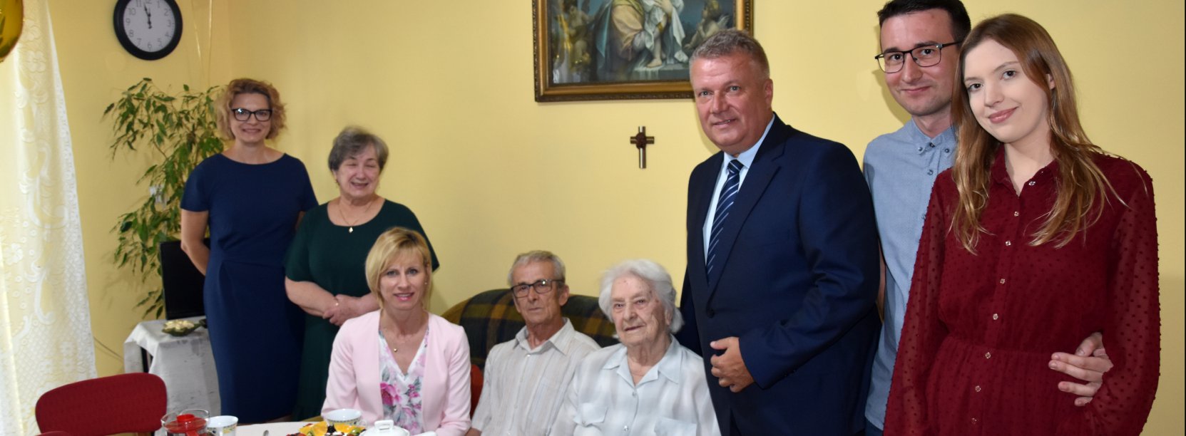 Stulatka siedząca przy stole, obok niej kilka uśmiechniętych osób 