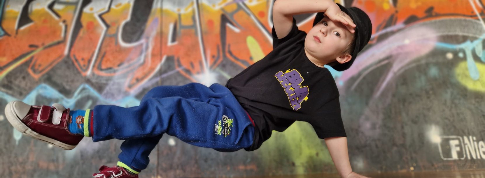 Młody chłopak tańczący breakdance, z tyłu graffitti