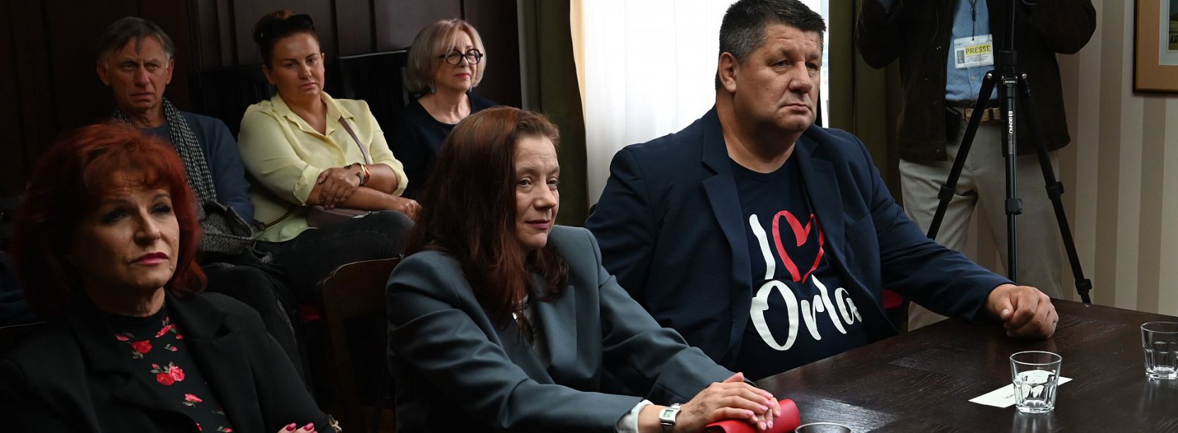 Sześc osób siedzących przy stole, obok kamera