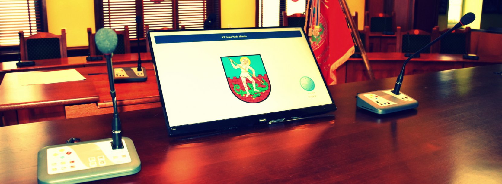 Sala obrad rady miejskiej, na pierwszym planie monitor wyświetlający herb miasta