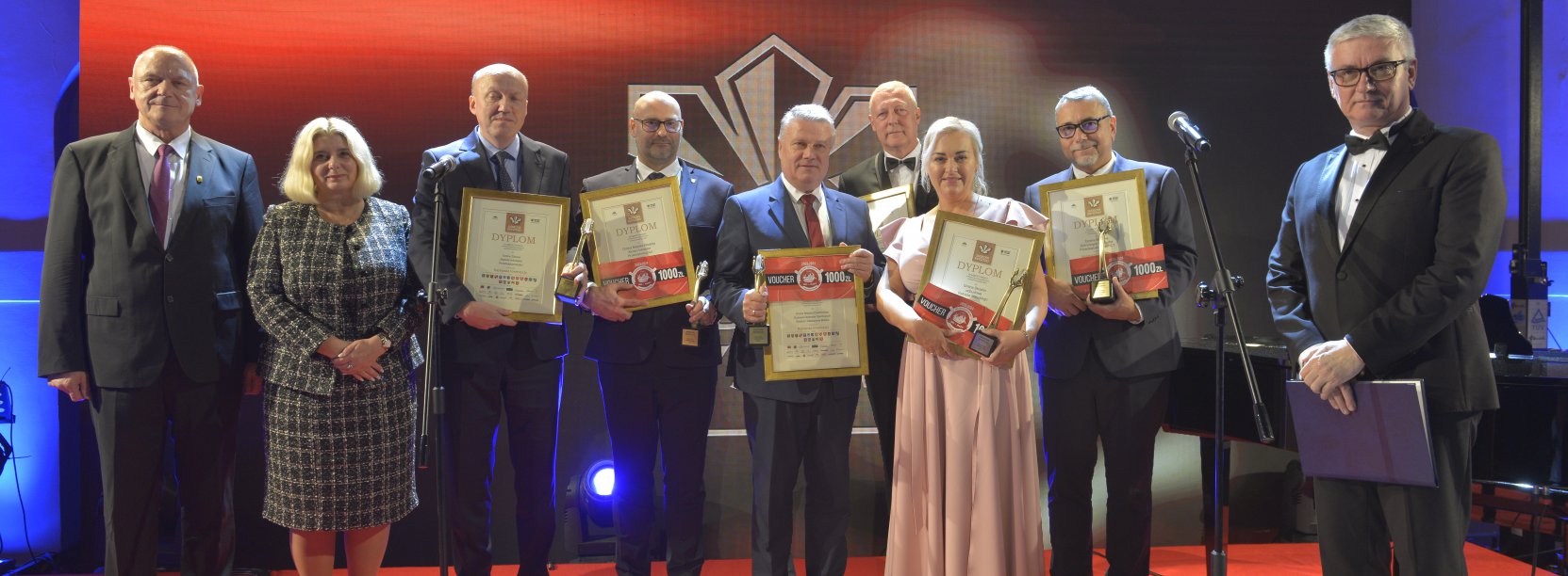 Grupa kobiet i mężczyn pozuje do wspólnego zdjęcia, czerwone tło