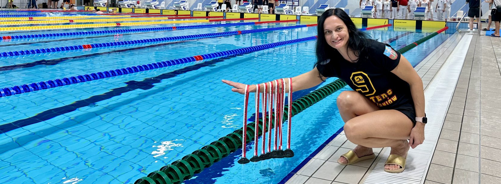 Dziewczyna kucająca przy krawędzi basenu krytego i trzymająca pęk medali
