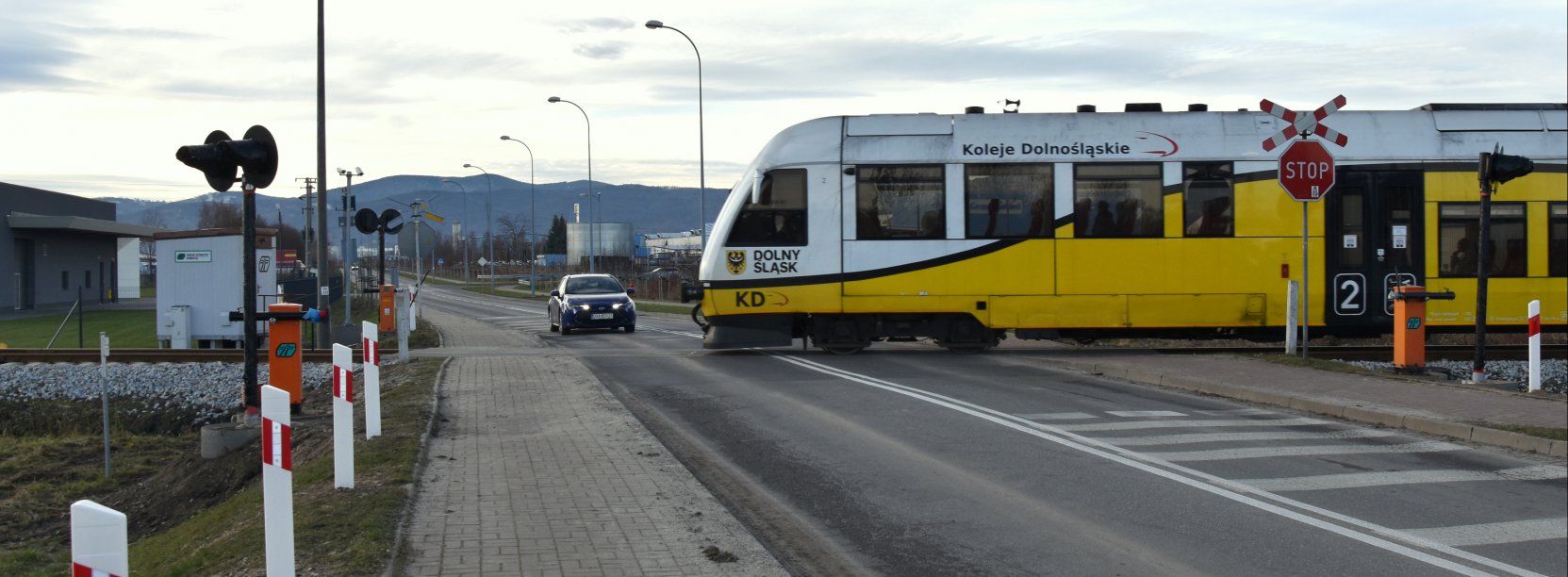 Szynobus, za nim samochód osobowy, w tle góry