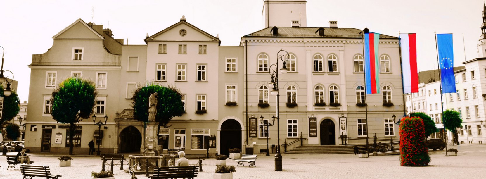 Budynek ratusza, przed nim trzy masty i flagi Polski, UE i Dzierżoniowa