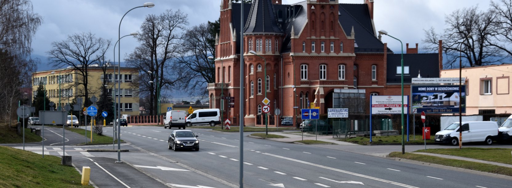 Szeroka droga, obok duża kamienica z czerwonej cegły