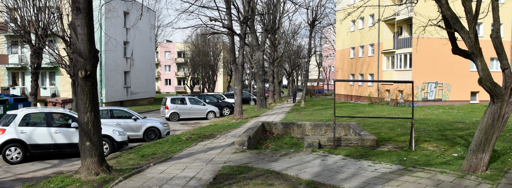 Osiedle, chodnik, obok zaparkowane auta,. w drugim planie bloki mieszkalne