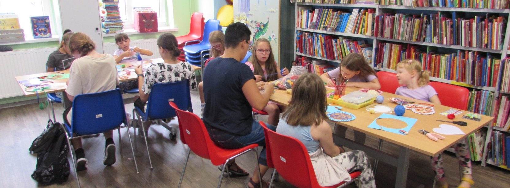 Grupa dzieci maluje przy dwóch stołach w bibliotece