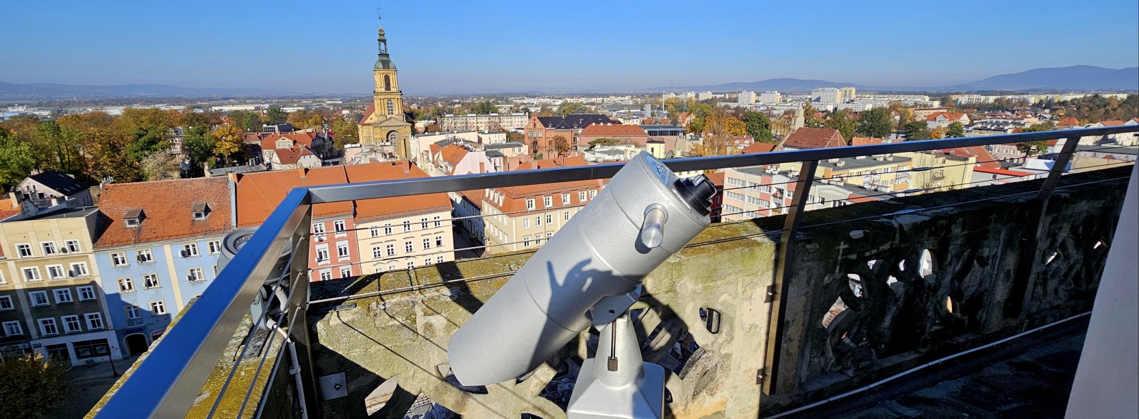Wieża ratuszowa z kamiennymi i metalowymi barierkami, na pierwszym planie luneta, w tle panorama miasta