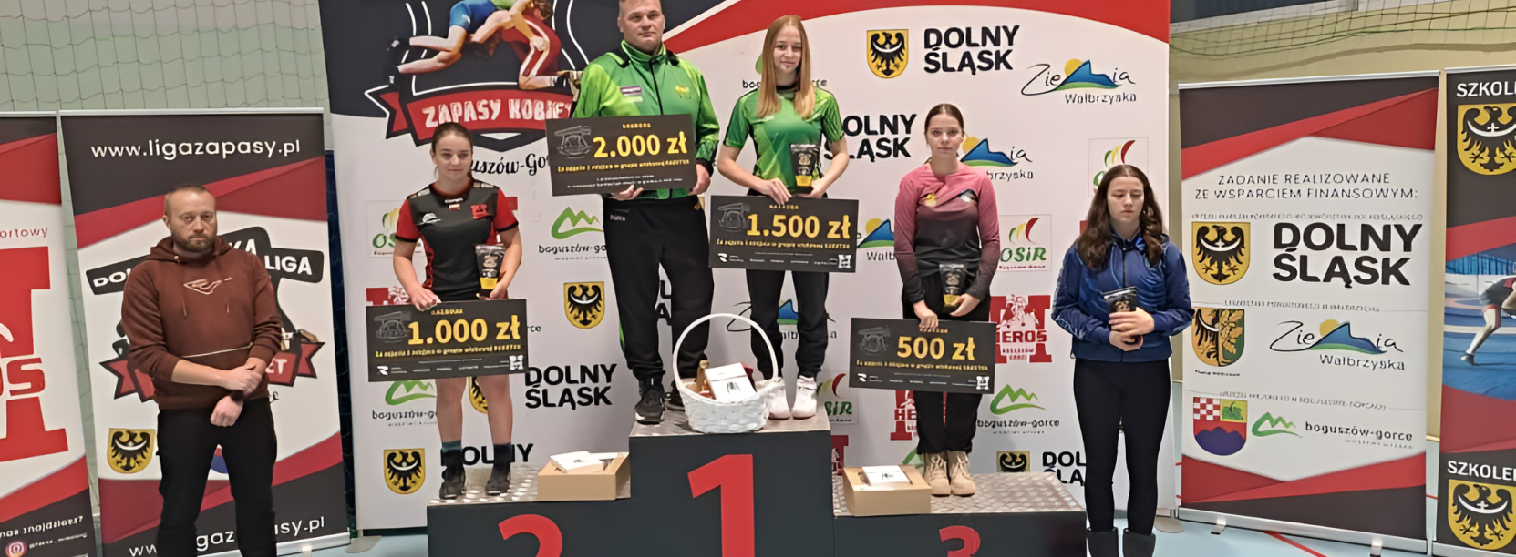 Zapaśniczki stojące na podium z symbolicznymi czekami