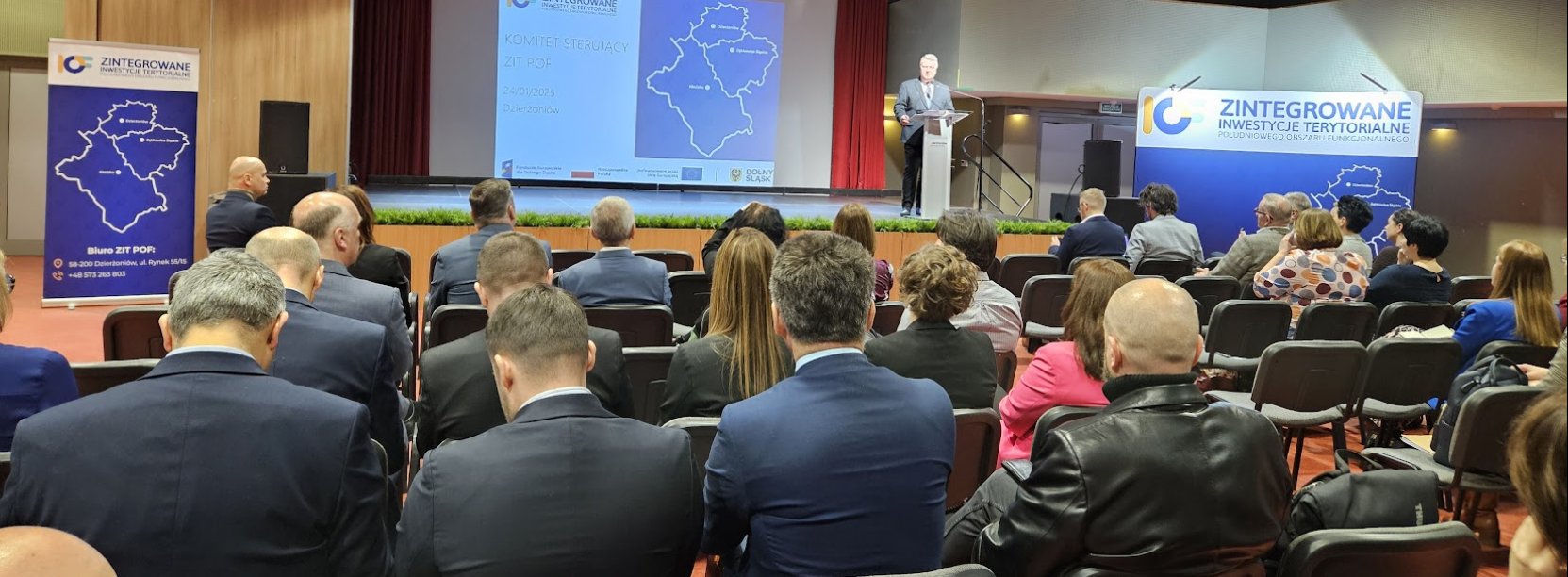 grupa ludzi na konferencji, w tle przemawia burmistrz Kucharski