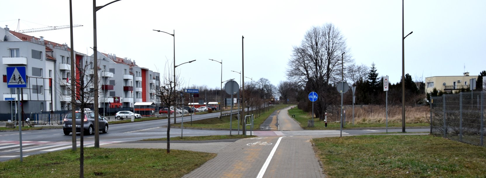 Szeroka ścieżka rowerowa przy drodze wyjazdowej z miasta, po lewej bloki mieszkalne