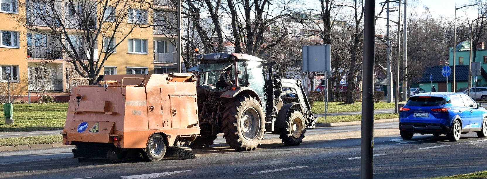 Maszyna zamiataqjąca drogę w mieście podczas ruchu samochodów