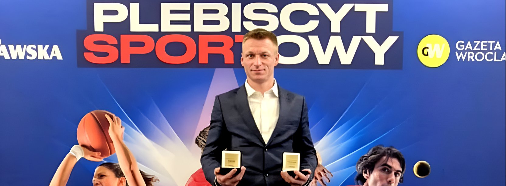 Patryk Ciszewski ze statuetkami w dłoniach, za nim napis Plebiscyt Sportowy