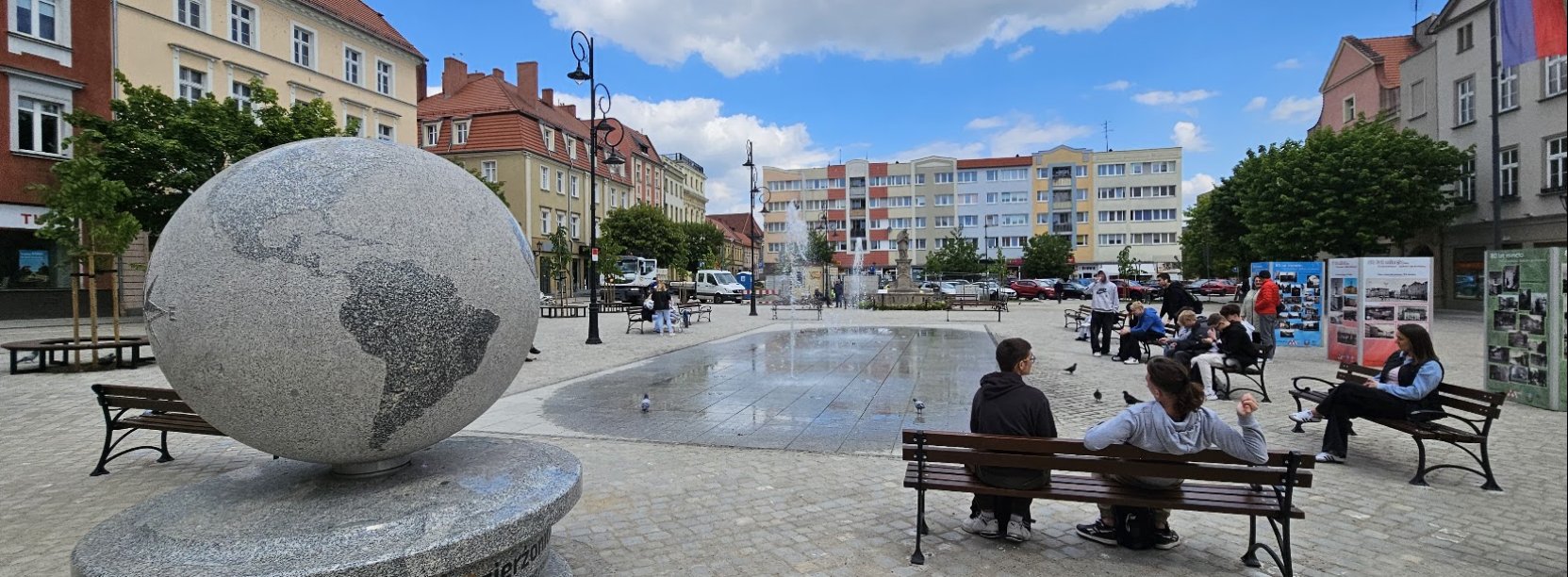 Rynek, ludzie siedzący na ławkach, po lewej ogromny kamienny globus