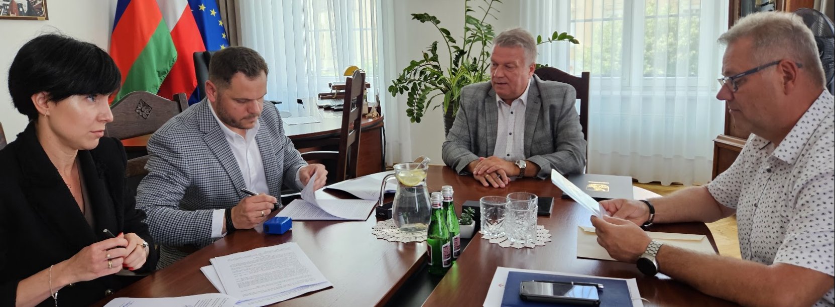 Cztery osoby, w tym burmistrz miasta Dariusz Kucharski (w środku), podpisują dokumenty przy stole w gabinecie burmistrza Dzierżoniowa