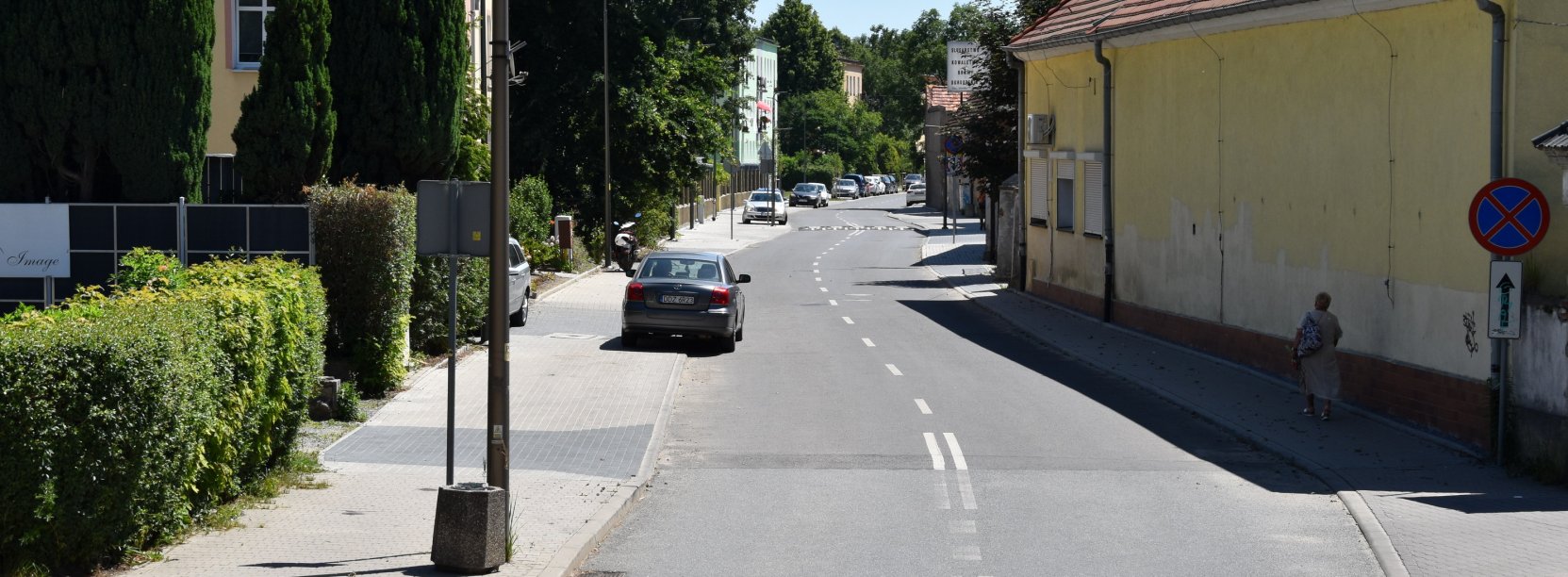 Ulica Słowiańska, na pierwszym planie przejście dla pieszych, na chodniku po lewej zaparkowane auta, obok zieleń