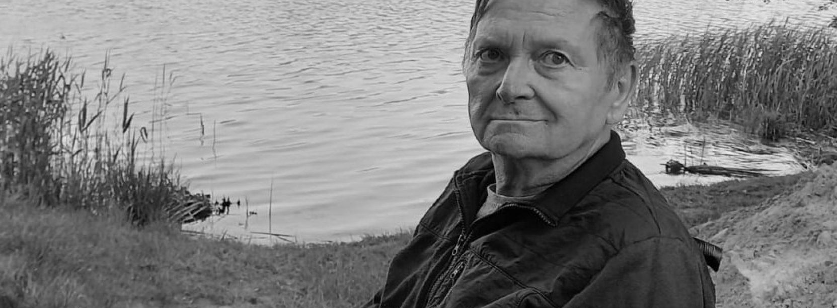Czarno-białe zdjęcie mężczyzny na wózku inwalidzkim, w tle zbiornik wodny