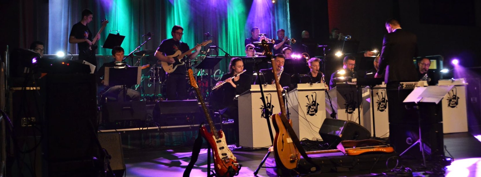Muzycy Big Roll Band na oświetlonej scenie, pzred nimi dyrygent i instrumenty