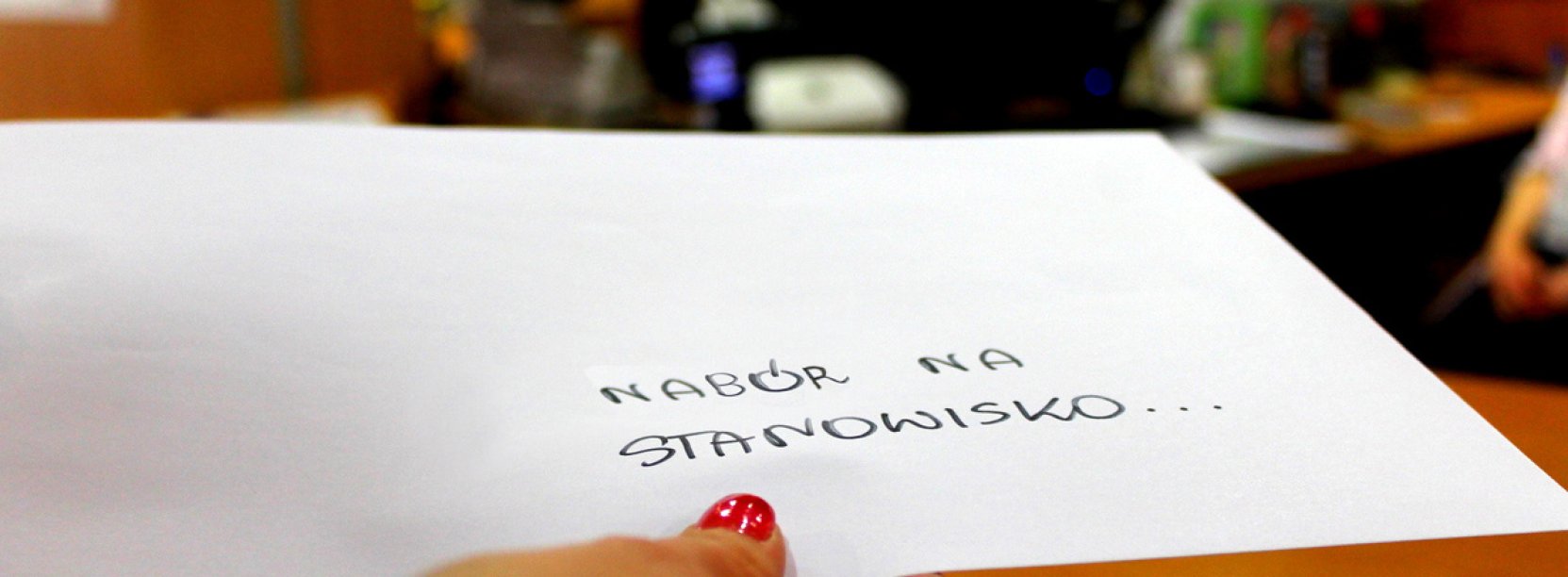 Ręka z kopertą z napisem "Nabór na stanowisko" na tle Biura Obsługi Klienta