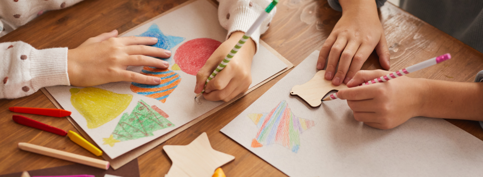 Ręce siedzących przy stole dzieci rysujących świąteczne elementy na kartkach papieru