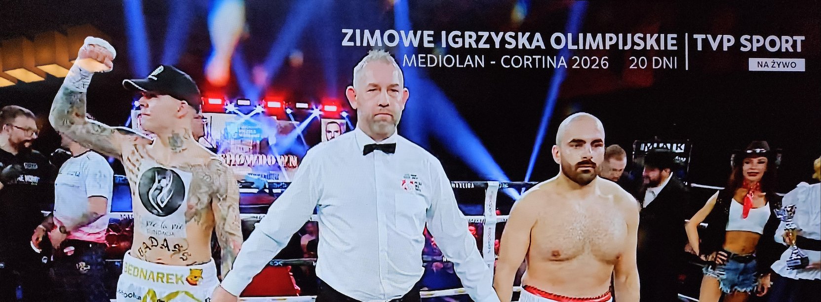 Ring bokserski, po wygranej walce dwaj bokserzy z sędzią, Kamil Bednarek unosi zaciśniętą rękę do góry w geście zwycięstwa