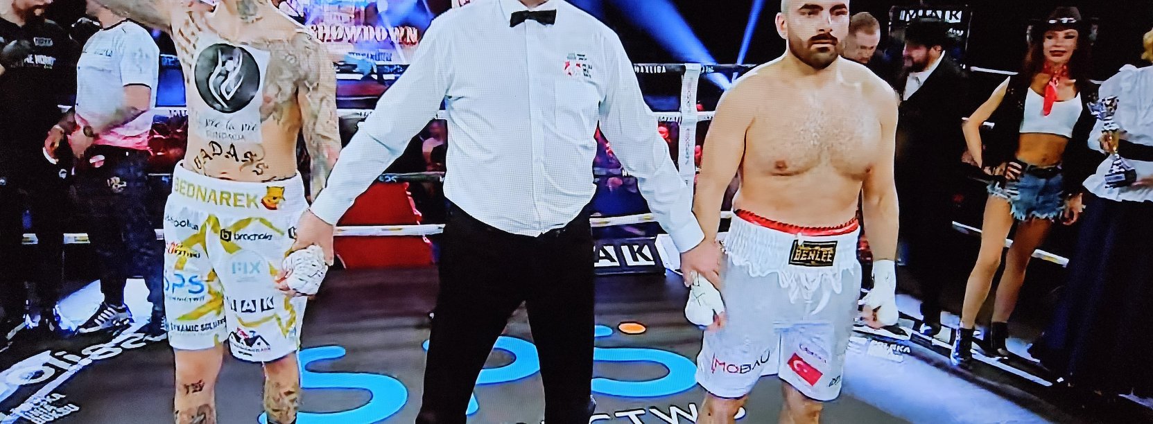 Ring bokserski, po wygranej walce dwaj bokserzy z sędzią, Kamil Bednarek unosi zaciśniętą rękę do góry w geście zwycięstwa