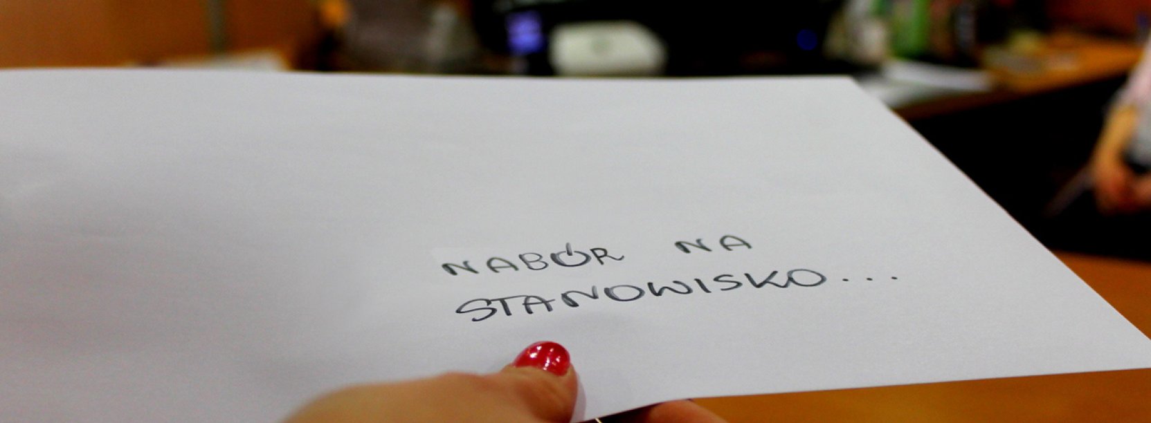 Zdjęcie ręki trzymającej kopertę z napisem "Nabór na stanowisku..." na tle Biura Obsługi Klienta