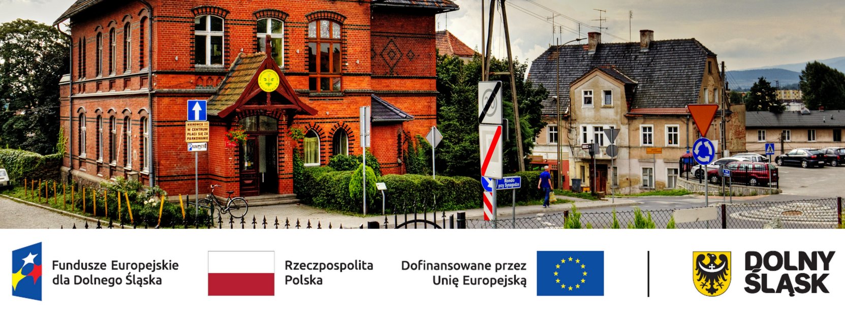 Budynek z czerwonej cegły, u dołu logotypy partnerów projektu