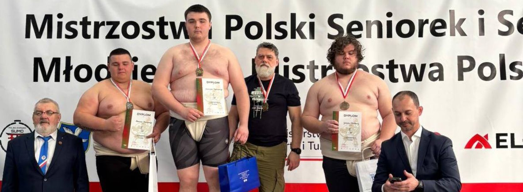 Zawodnicy sumo stojący na podium na biało-czerwonym tle