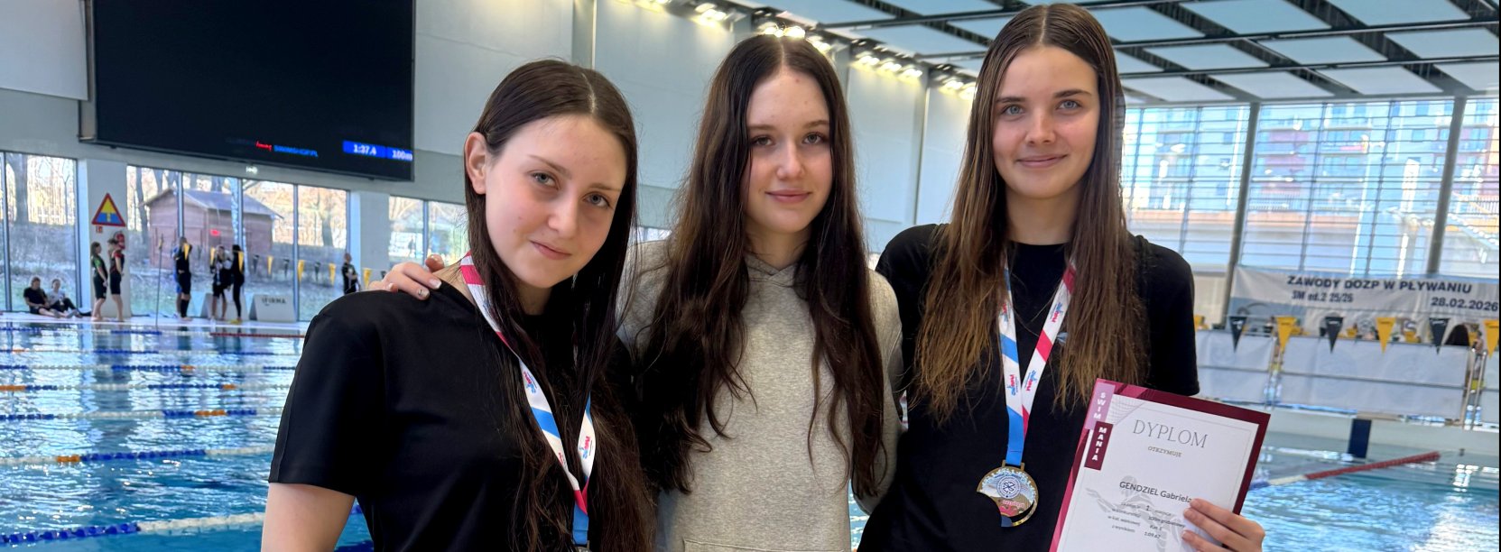 Trzy pływaczki, w tym dwie z dyplomami, na tle basenu