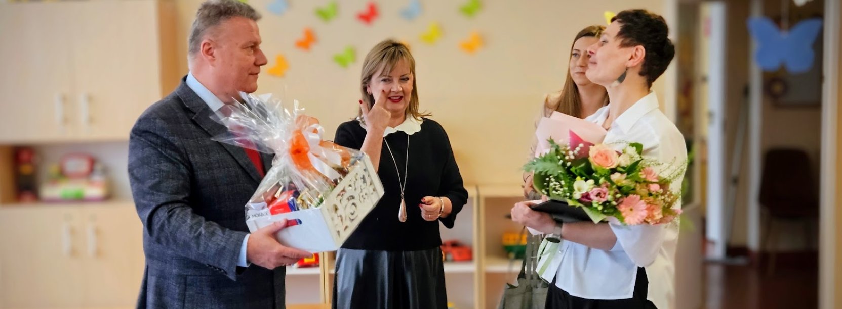 Burmistrz wręczający dyrektorce żłobka kwiaty i biały koszyk ze słodyczami