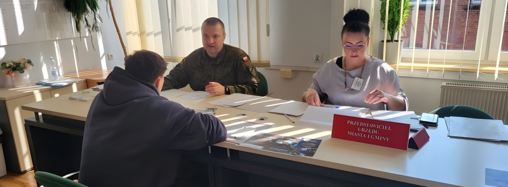 Żołnierz w mundurze i kobieta siedzący przy stole, przed nimi młody człowiek w bluzie z kapturem