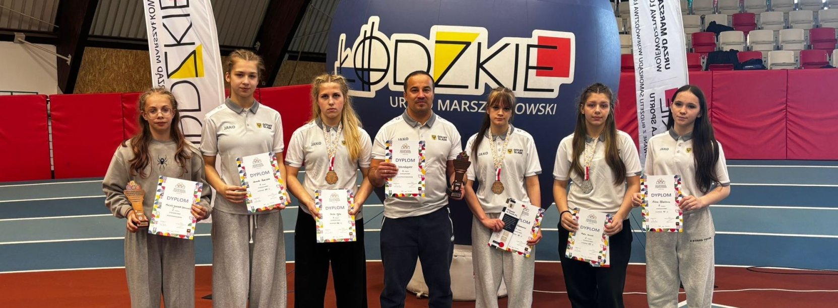 Sześć zapaśniczek w hali sportowej, pośrodku trener