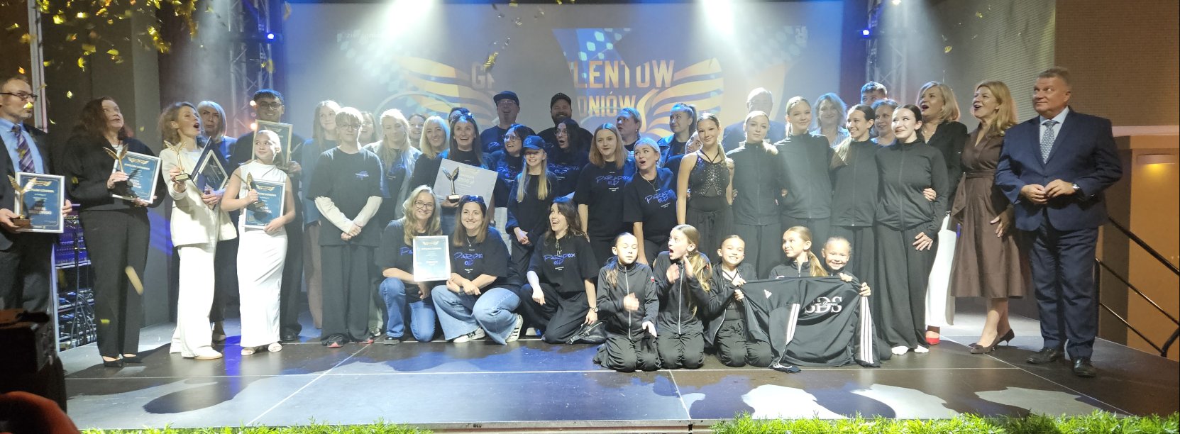 Wszyscy laureaci na wspólnym zdjęciu na scenie patrzą na lecące z góry konfetti