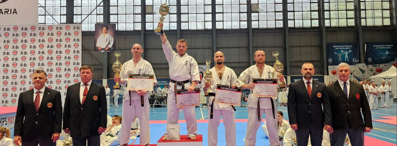 Czwórka zawodników w strojach do karate stoi na podium. Na najwyższym stopniu Tomasz Staściuk z uniesionym do góry pucharem