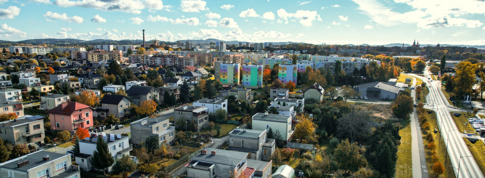 Miasto z góry, na pierwszym planie domki jednorodzinne, za nimi osiedla, dalej góry 